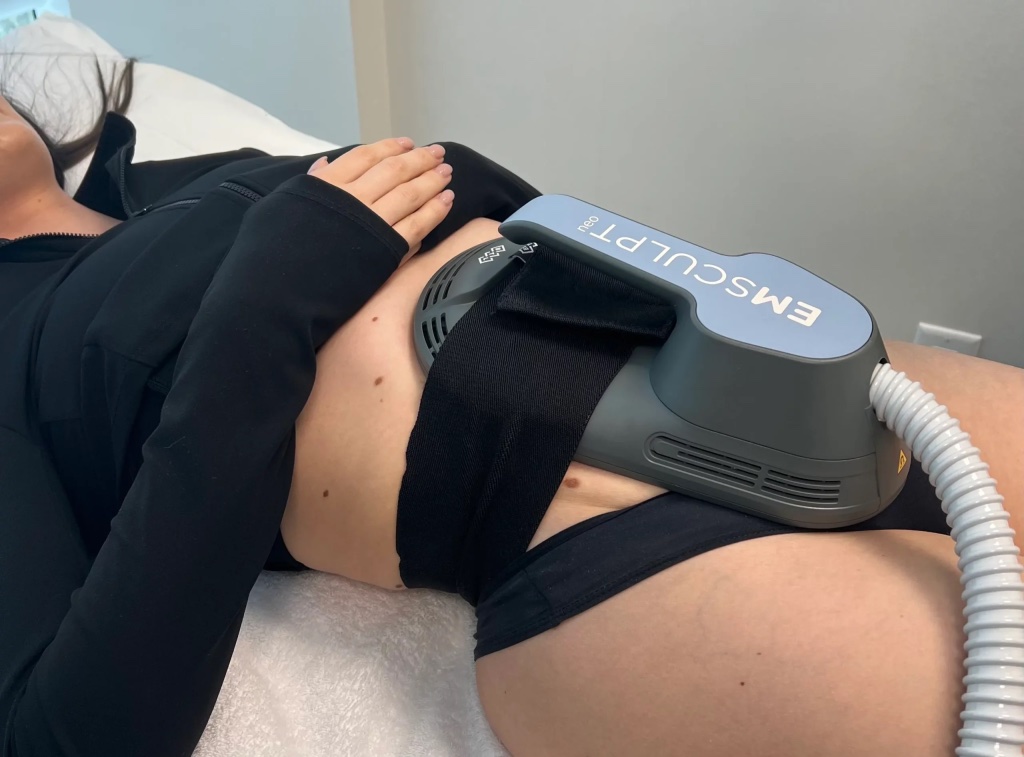 Emsculpt Neo applicator strapped across a client's abdomen during a HIFEM session at Sculpted Body Curves